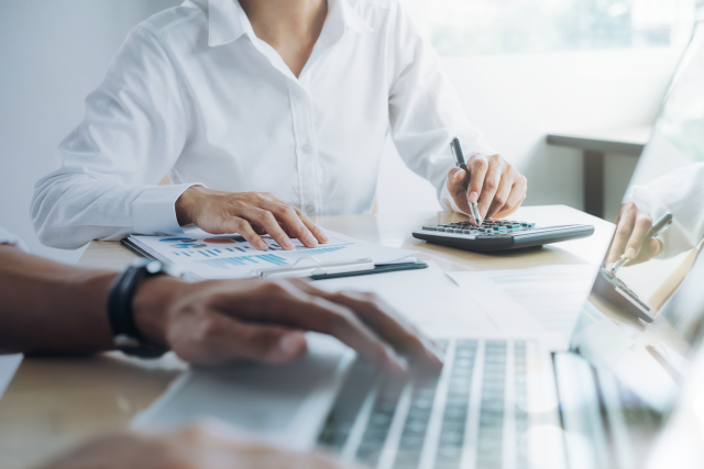 an individual working on their laptop while another uses their calculator