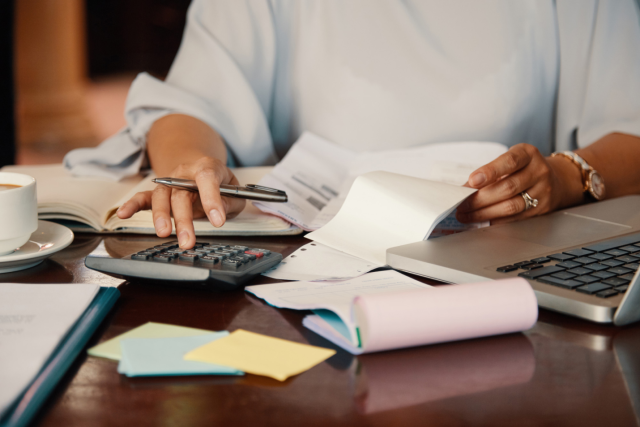 a person working on a calculator while holding multiple documents